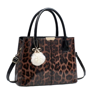 Stylish leopard print handbag with glossy finish, dual handles, and plush charm