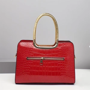 Details der roten Lacktasche mit Krokoprägung und goldenem geflochtenem Metallgriff