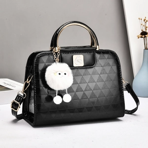Detail of black glossy embossed handbag featuring golden metal handles and a plush monster charm