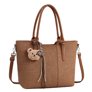 Brown woven tote bag with leather handles and a cute plush bear pendant on white background