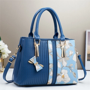 Detail of floral embroidery on blue leather handbag with elegant bow pendant and gold hardware