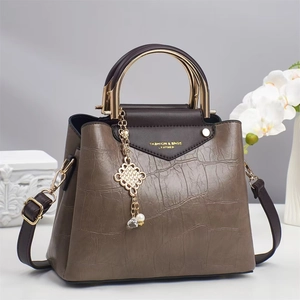 Detalle de bolso en piel con relieve de cocodrilo marrón y asa de metal dorado