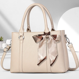 Details der beigen Handtasche aus genarbtem Leder mit Silberbeschlägen und Seidenschleife
