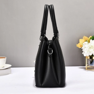 Detail of black litchi leather tote bag side view with pearl and chain charm accessory