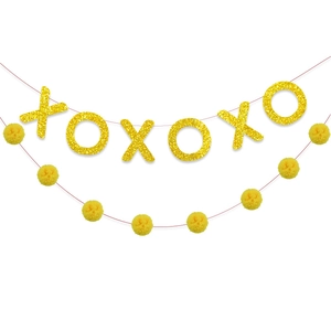 Dettaglio di lettere XOXO glitterate e pompon gialli su uno striscione decorativo