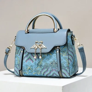 Sac à main brodé bleu avec boucle cygne doré et pendentif perle sur support blanc