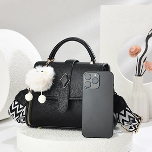 French style black pebble leather handbag with geometric strap and plush pendant on white display
