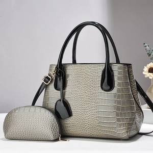 Detail of grey crocodile embossed handbag with glossy black handles and shoulder strap