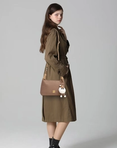 Close-up of brown textured shoulder bag with golden logo and white plush sheep pendant
