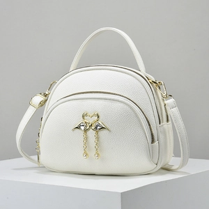 Detail of white pebbled leather bag featuring a gold flamingo heart and pearl tassel