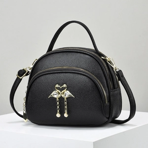 Detail view of black litchi leather handbag featuring a golden flamingo heart charm