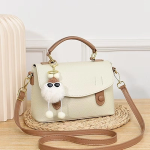 Minimalist beige leather satchel bag with brown handle and plush charm on a wooden desk