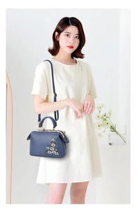 Detailed embroidery of white and pink flowers on a luxury dark blue shoulder bag