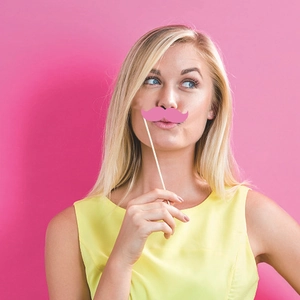 Hawaiian party photo booth prop set featuring a pink mustache held by a smiling model