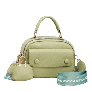 Green textured crossbody bag with broad woven strap and mini pouch charm on white background