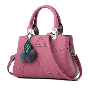Detail view of pink leather handbag featuring a metal logo, green leaf and gray fur pompom charm