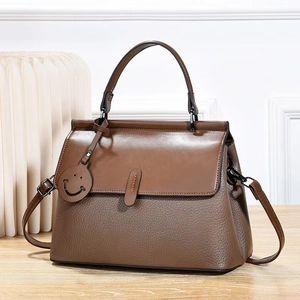 Brown leather trapezoid handbag with dual textures and adjustable strap on a wood surface