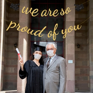 Detail of gold glitter 'we are so proud of you' graduation banner with mini black doctor caps