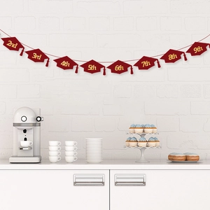 Graduation banner with burgundy cap cutouts and gold numbers on white brick wall