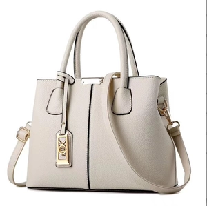 Macro view of creamy white lychee grain leather texture and metallic letter charm on bag
