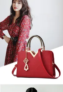 Close-up of red V-quilted handbag with gold metal trim and pearl charm detail