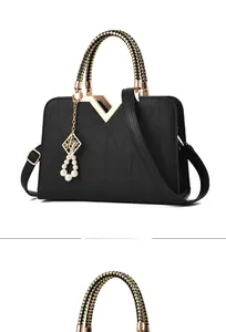 Detail of black quilted leather handbag with woven handle and pearl charm attachment