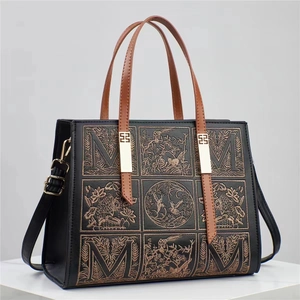 Close-up of bronze embroidery with bird and floral patterns on black leather tote bag