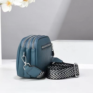Detail of teal pebble leather bag showing triple zip layers and geometric strap