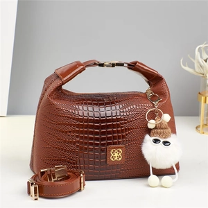 Piccola borsa a bauletto marrone a coccodrillo con logo a quadrifoglio e ciondolo peluche