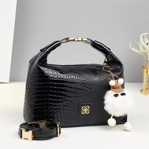 Dettaglio borsa in vernice nera coccodrillo con logo dorato e ciondolo peluche