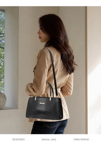 Detail of black crocodile texture handbag with gold hardware and shoulder strap