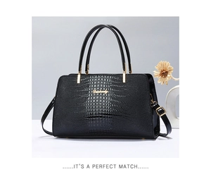 Detail view of black crocodile embossed handbag with gold hardware and logo on neutral backdrop