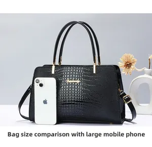 Detail view of large black crocodile embossed tote bag next to a smartphone for size scale