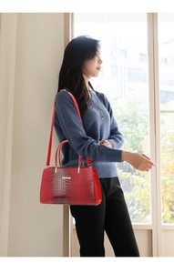 Detailed view of red crocodile-pattern tote bag with metallic logo and slim shoulder strap