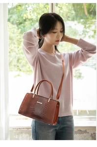 Detail of brown crocodile pattern handbag with dual handles and metal logo plaque