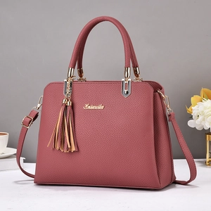 Pink lychee texture leather tote bag with gold hardware and tassel charm on a white desk