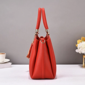 Detail of red pebbled leather tote bag featuring gold hardware and leather tassel