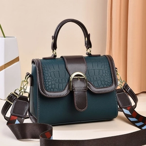 Detail of dark green crossbody bag with crocodile texture and geometric woven strap