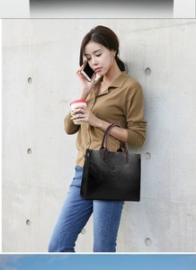 Close-up of a large black leather tote bag featuring elegant brown top handles for women