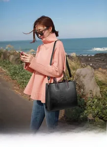 Detail of a black textured faux leather handbag with adjustable shoulder strap and handles