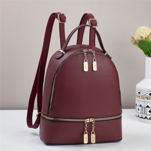 Detail eines weinroten Lederrucksacks mit goldenen Reißverschlüssen und zwei Fächern