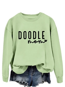 Detail of light green round neck sweatshirt featuring black Doodle Mom typography