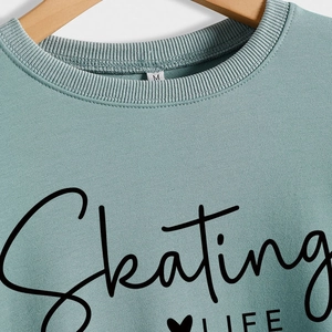 Sage green crewneck sweatshirt with black Skating Life heart print on wooden hanger
