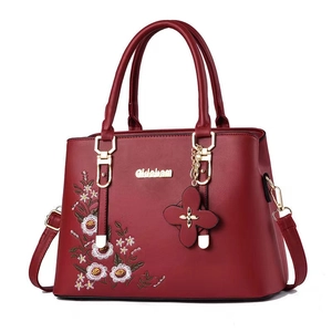Elegant dark red handbag with floral embroidery and gold hardware on white background
