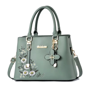 Elegant green handbag with daisy embroidery and gold hardware on white background