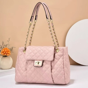 Pale pink quilted crossbody bag with gold chain strap and turn-lock closure on white stand