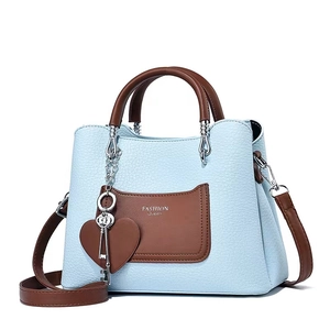 Elegant light blue leather handbag with brown handles and heart pendant on white background
