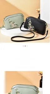 Detail view of floral embroidery on leather crossbody bag with dual golden zippers