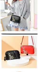 Detail of floral embroidery on black and red crossbody bags with golden hardware