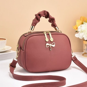 Detail of mauve lychee grain leather handbag with ruffled handle and bow charm